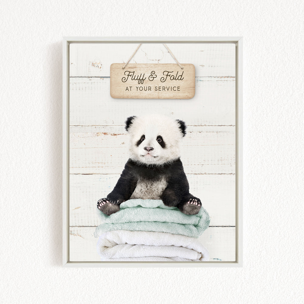 A panda bear sitting on a stack of towels, with a wooden sign above that says "Fluffy & Fold at your service".