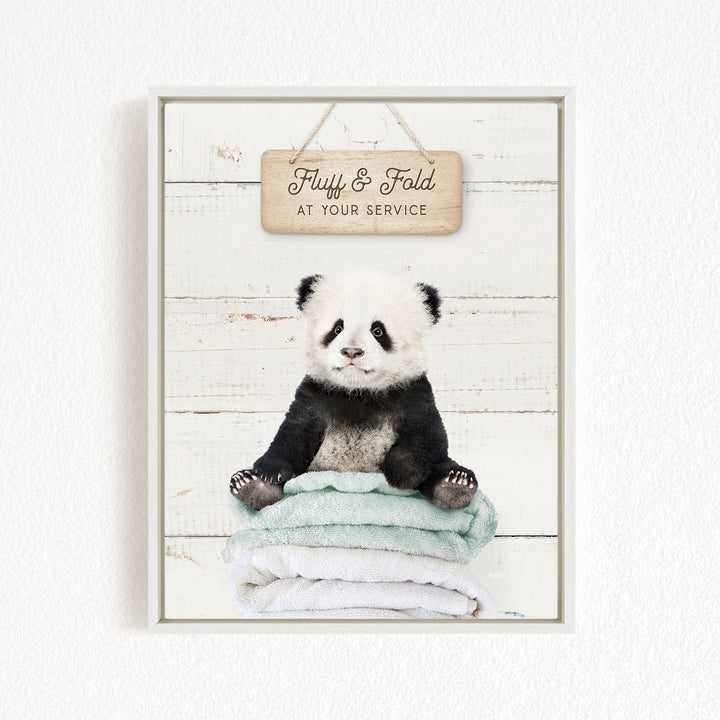 A panda bear sitting on a stack of towels, with a wooden sign above that says "Fluffy & Fold at your service".