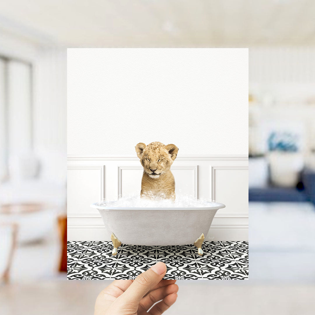 A young lion cub sitting in a white bathtub filled with water, surrounded by a black and white patterned floor.