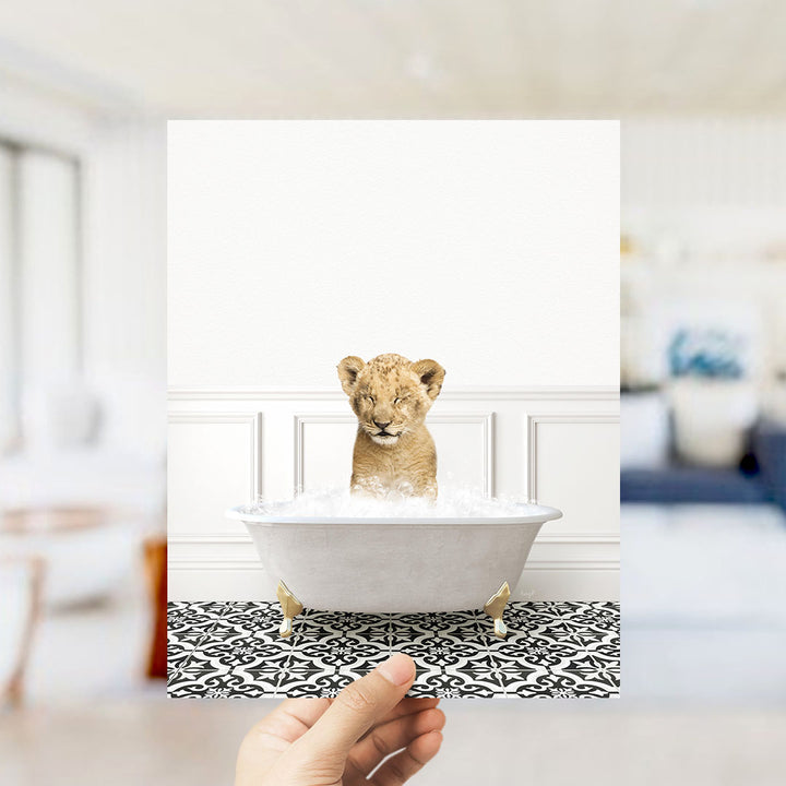 A young lion cub sitting in a white bathtub filled with water, surrounded by a black and white patterned floor.
