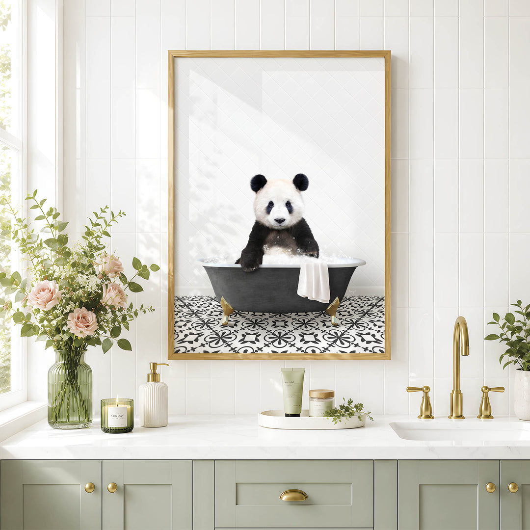 A framed image of a panda sitting in a bathtub is displayed on a white tiled wall above a bathroom counter with various toiletries and a vase of flowers.