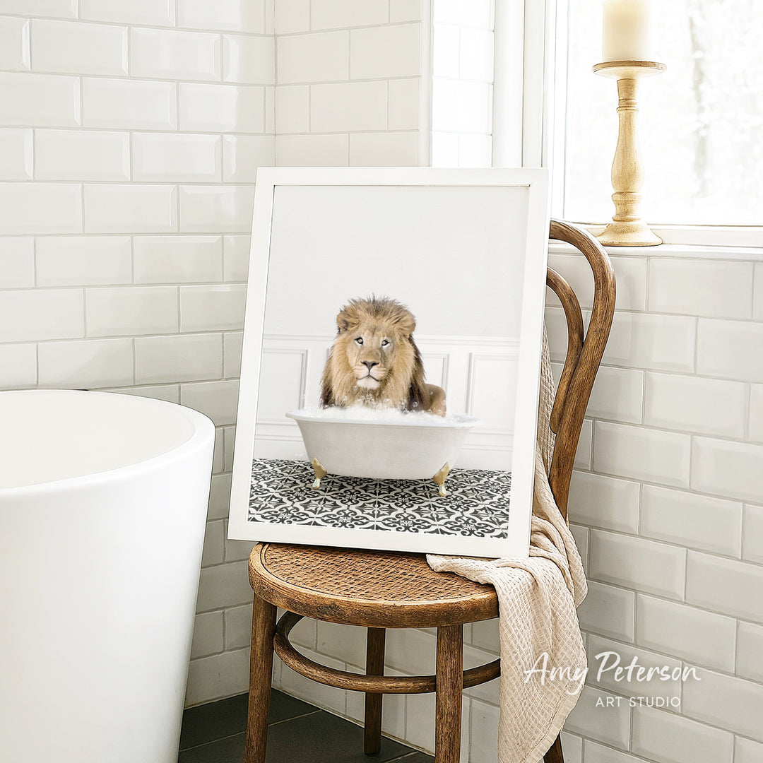 A framed image of a lion sitting in a bathtub, with a towel draped over the back of a chair in a bathroom setting.