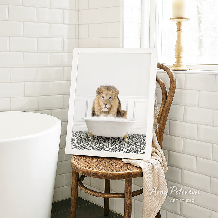 A framed image of a lion sitting in a bathtub, with a towel draped over the back of a chair in a bathroom setting.