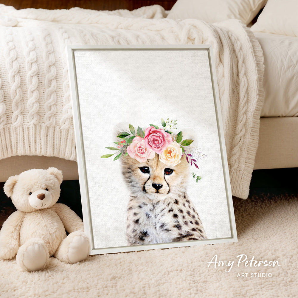 A framed print of a cheetah wearing a floral crown is displayed on a beige carpet, accompanied by a teddy bear.