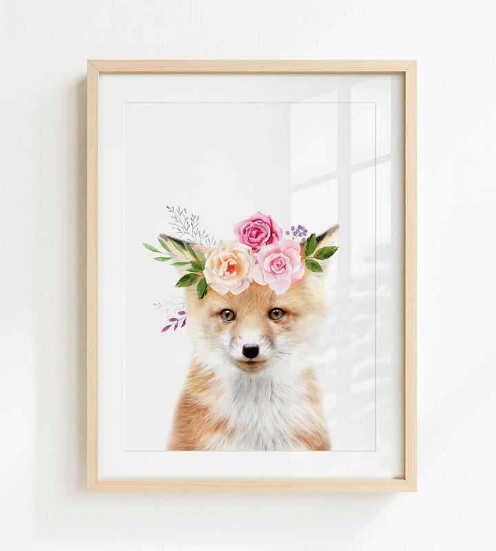 A framed print of a fox wearing a floral crown of pink and white roses and greenery.