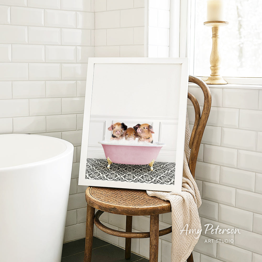 A framed image of two small dogs sitting in a pink bathtub, with a wooden chair and a white tiled wall in the background.
