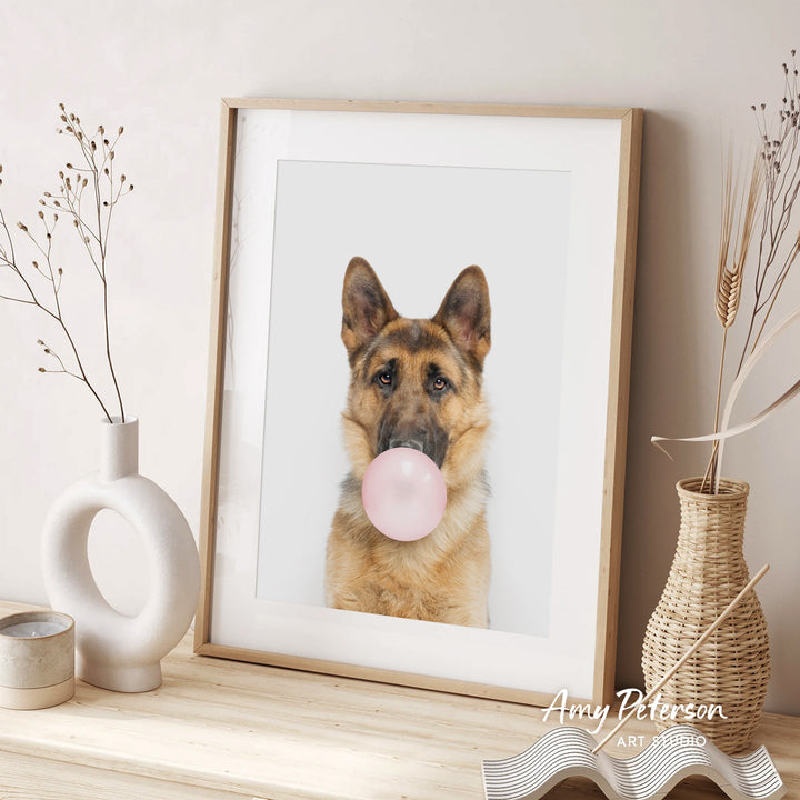 A framed photograph of a German Shepherd dog blowing a bubble with a pink bubble gum bubble, accompanied by decorative vases and a text that reads " Amy Peterson ART STUDIO".