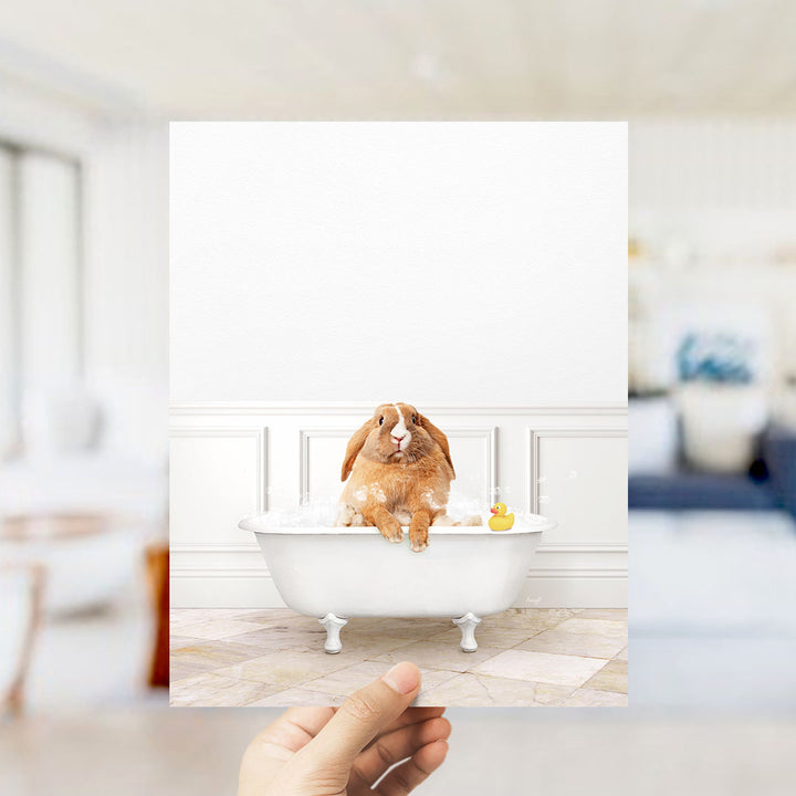 A brown rabbit sitting in a white bathtub filled with bubbles, with a yellow rubber duck floating nearby.