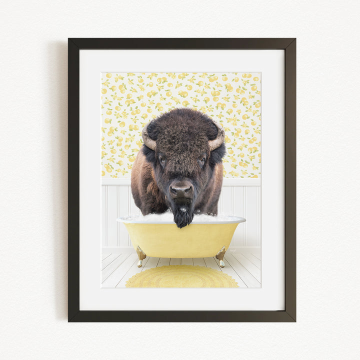 A buffalo with a black mane and horns is sitting in a yellow bathtub, with a yellow floral wallpaper behind it.