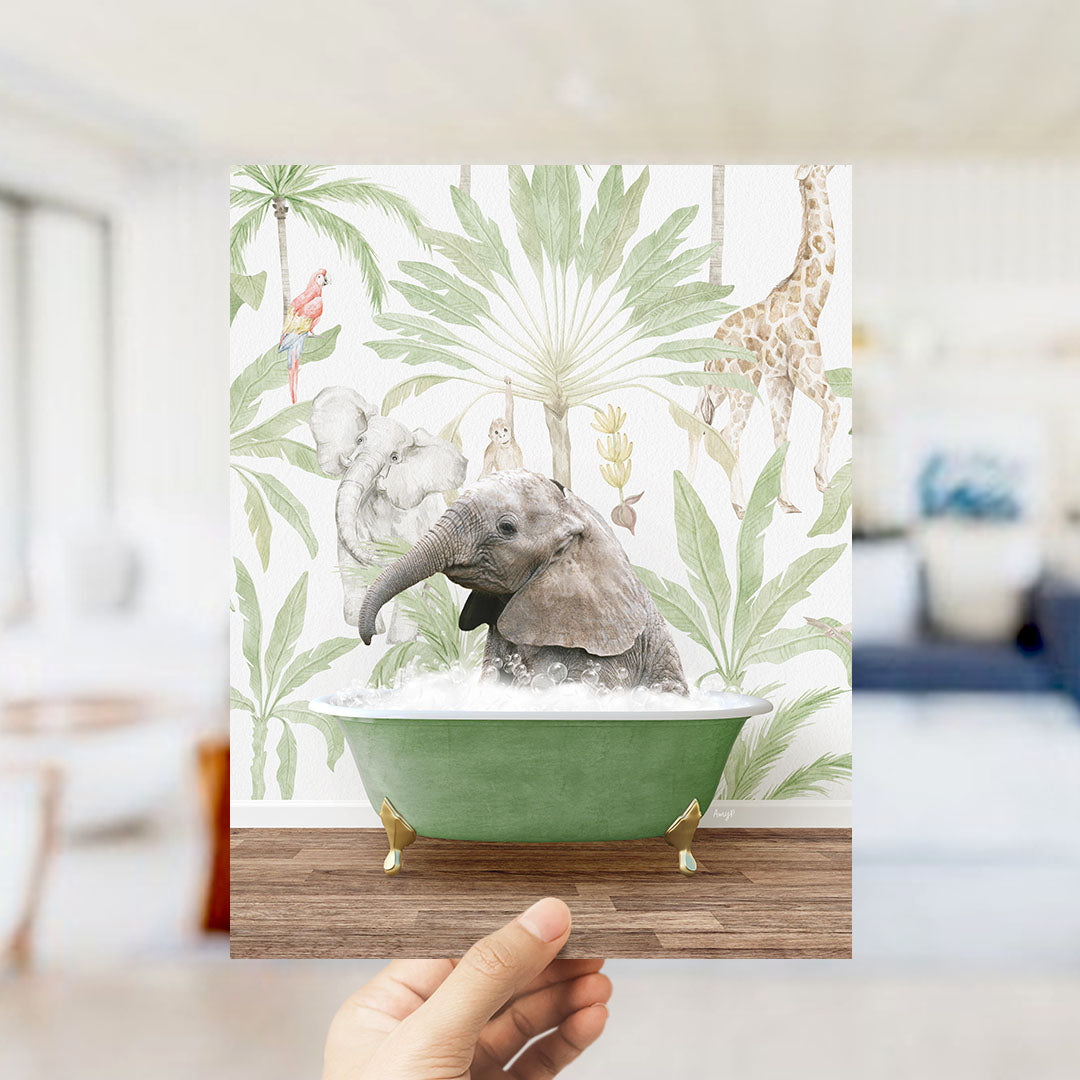 A hand holds up a framed image depicting a baby elephant sitting in a green bathtub, surrounded by tropical foliage and animals.