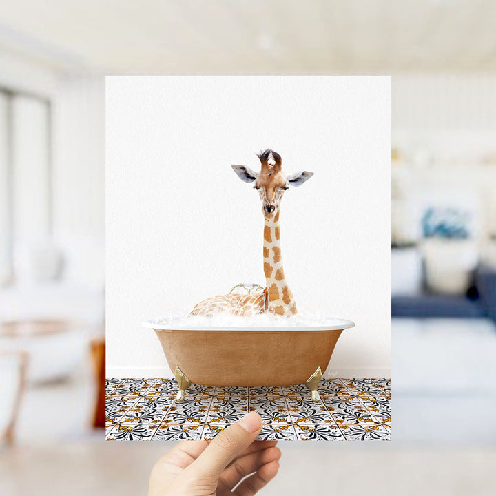 A giraffe sitting in a bathtub filled with bubbles, with a hand holding the photo up to the camera.