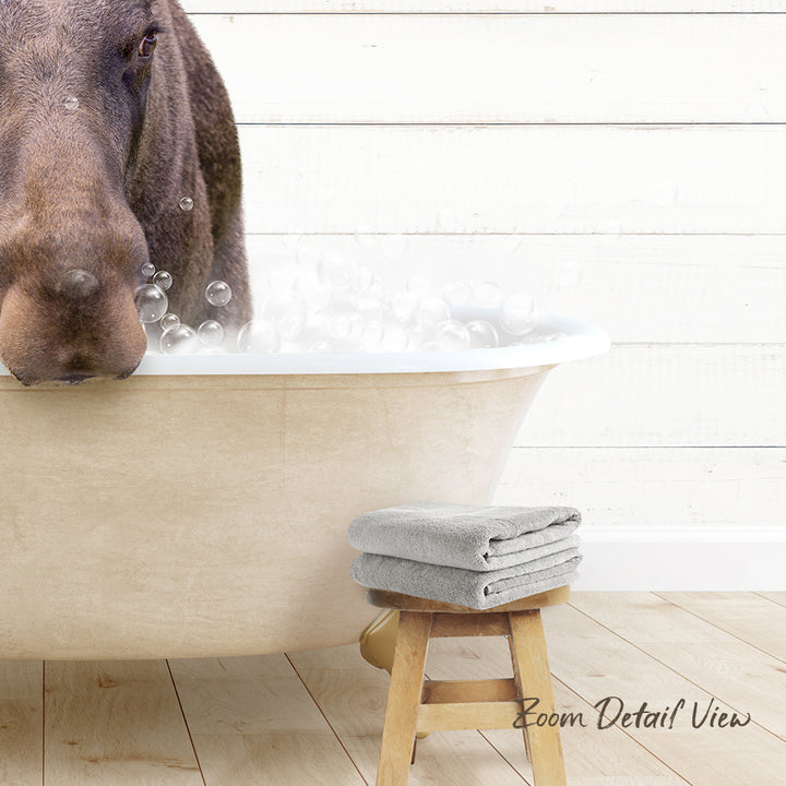 A dog is standing in a bathtub filled with bubbles, with a towel and stool nearby.