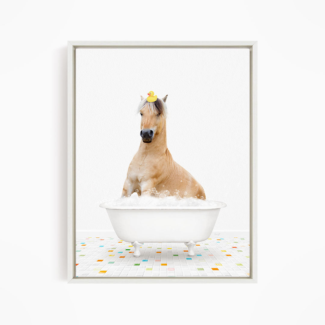 A light brown horse is sitting in a white bathtub filled with bubbles, with a yellow rubber duck perched on its head.