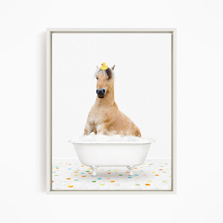 A light brown horse is sitting in a white bathtub filled with bubbles, with a yellow rubber duck perched on its head.