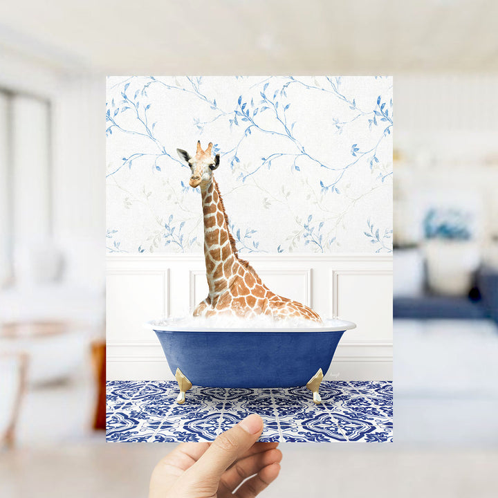 A giraffe sitting in a blue bathtub filled with bubbles, surrounded by a blue and white floral patterned wall.