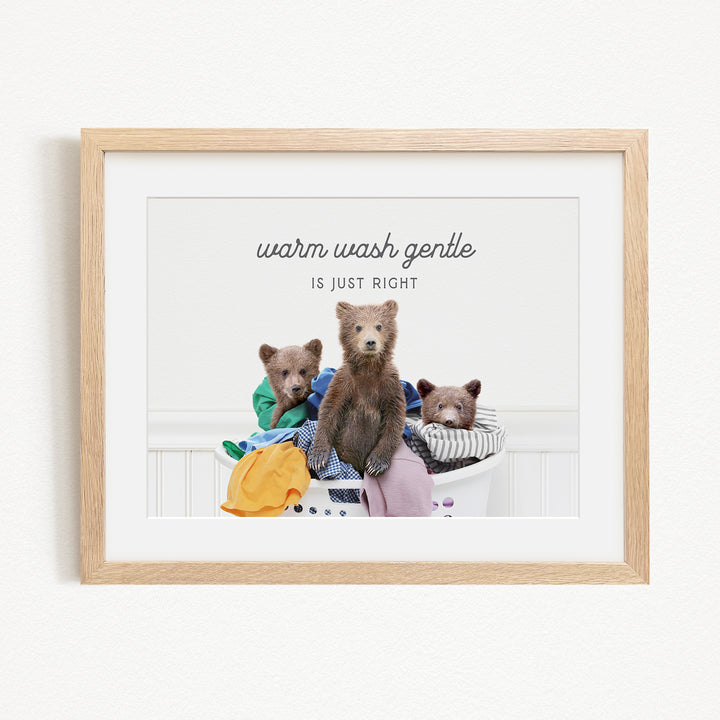 A framed image depicting three bears sitting in a laundry basket, with the text "Warm wash gentle is just right" written above them.