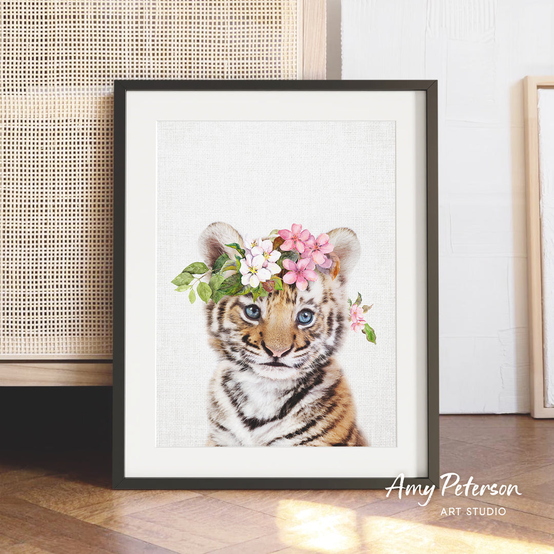 A framed print of a tiger cub wearing a floral headpiece is displayed on a wooden floor.
