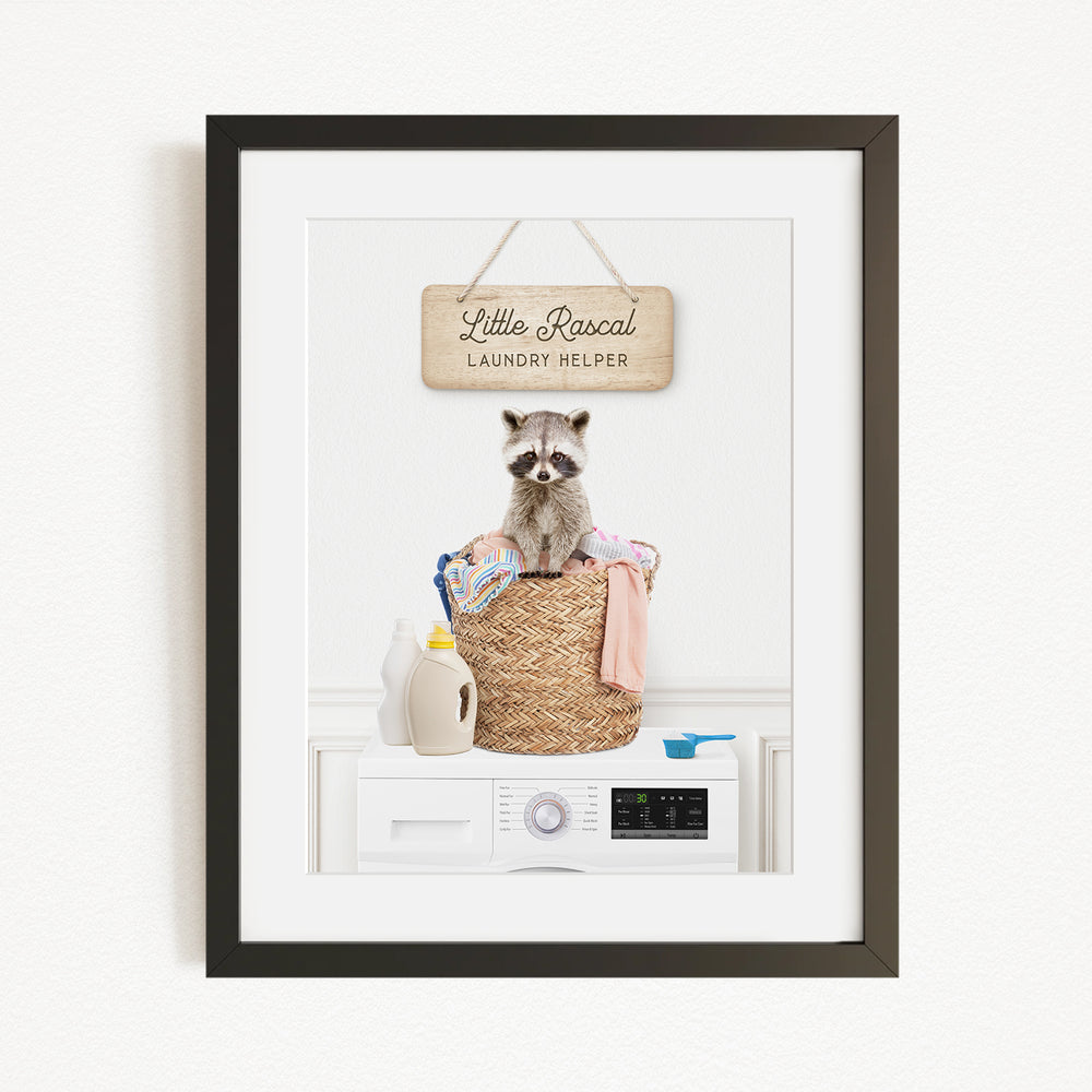 A raccoon sitting in a laundry basket, with a sign above that says "Little Racquel Laundry Helper".