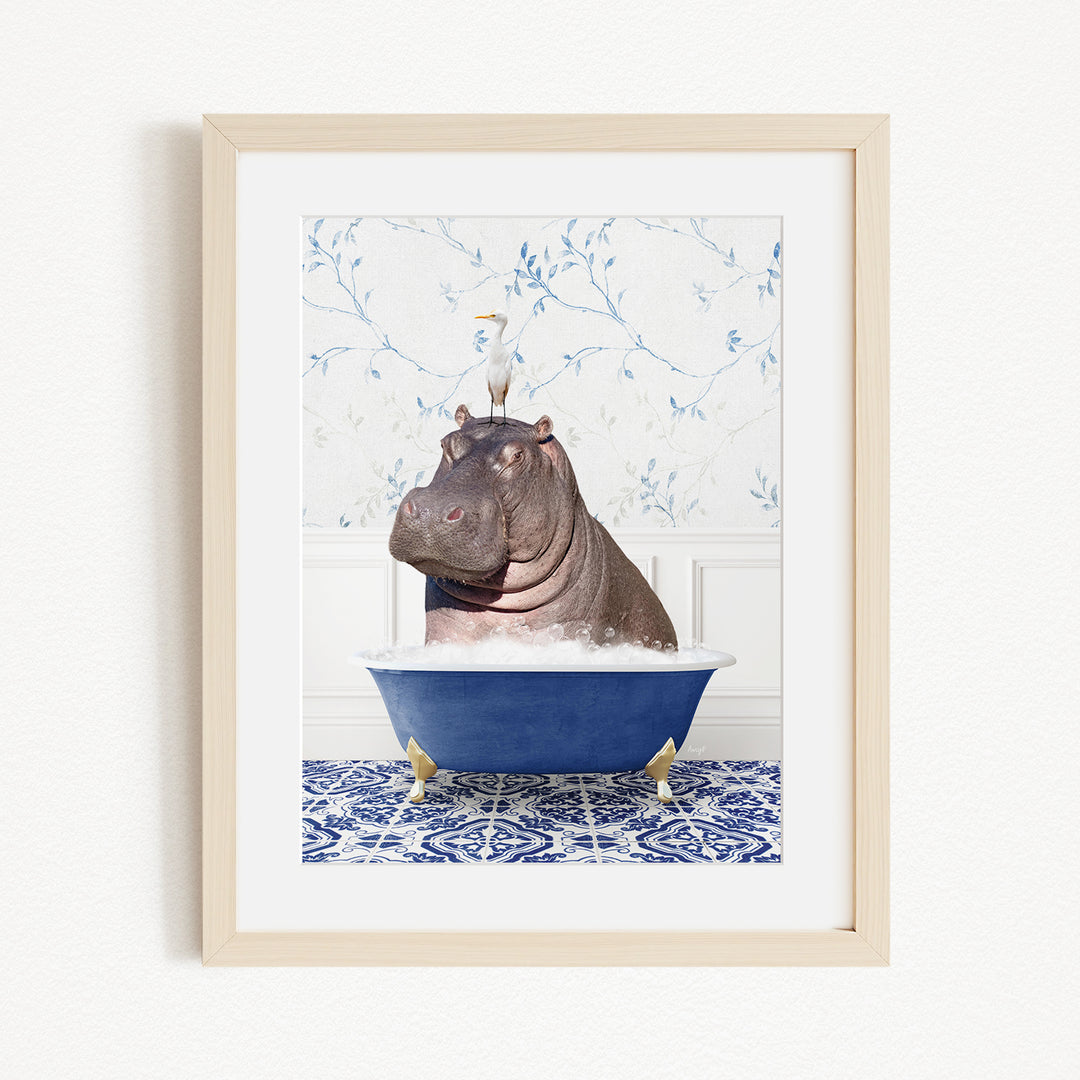 A framed image depicting a hippopotamus sitting in a blue bathtub, with a bird perched on its head.
