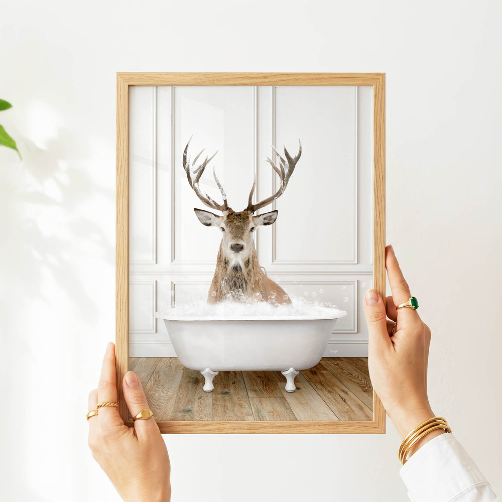 A person's hands are holding a picture frame with a photograph of a deer sitting in a bathtub.