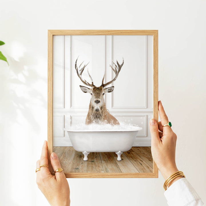 A person's hands are holding a picture frame with a photograph of a deer sitting in a bathtub.