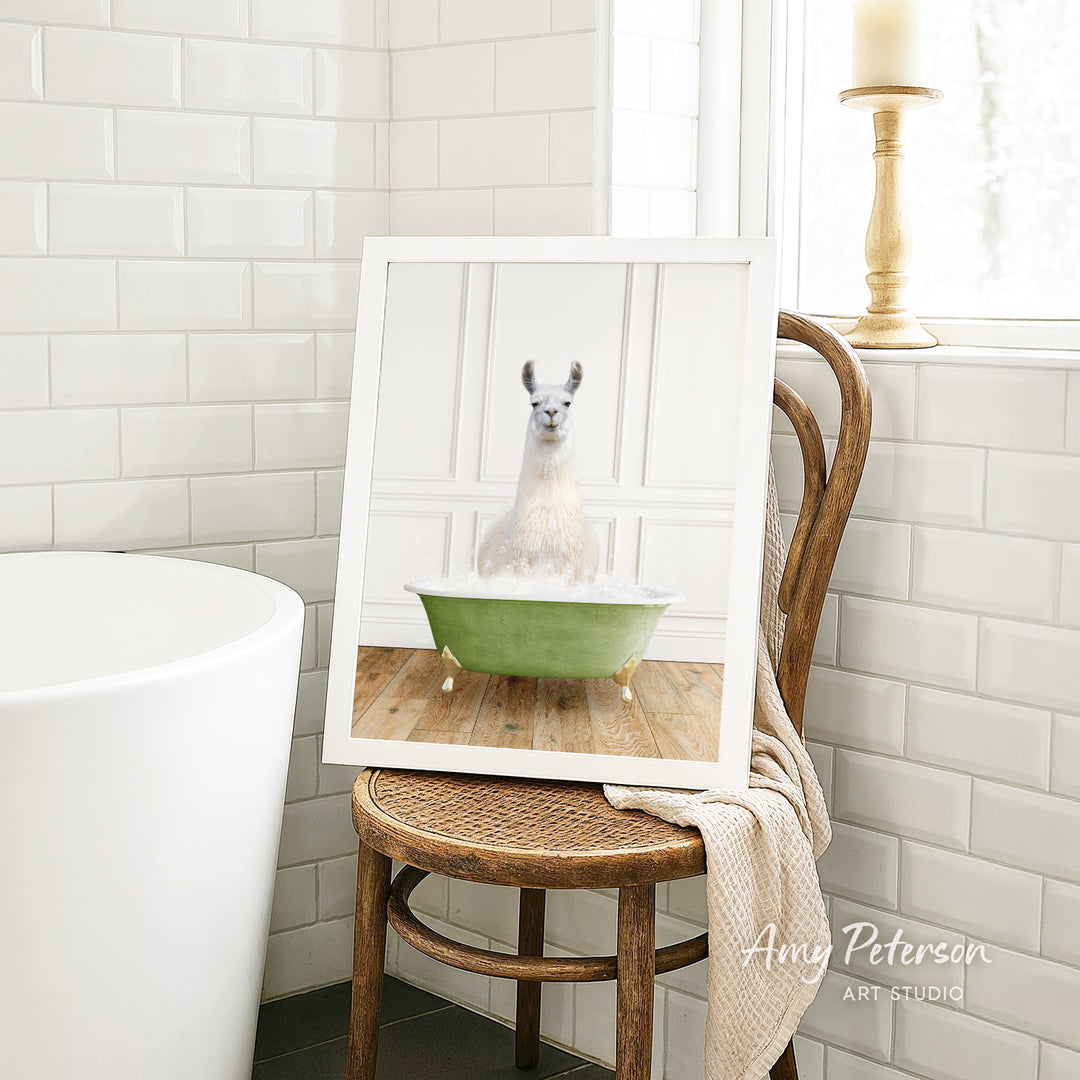 A framed image of a white llama sitting in a green bathtub, with a wooden chair and a white tiled wall in the background.