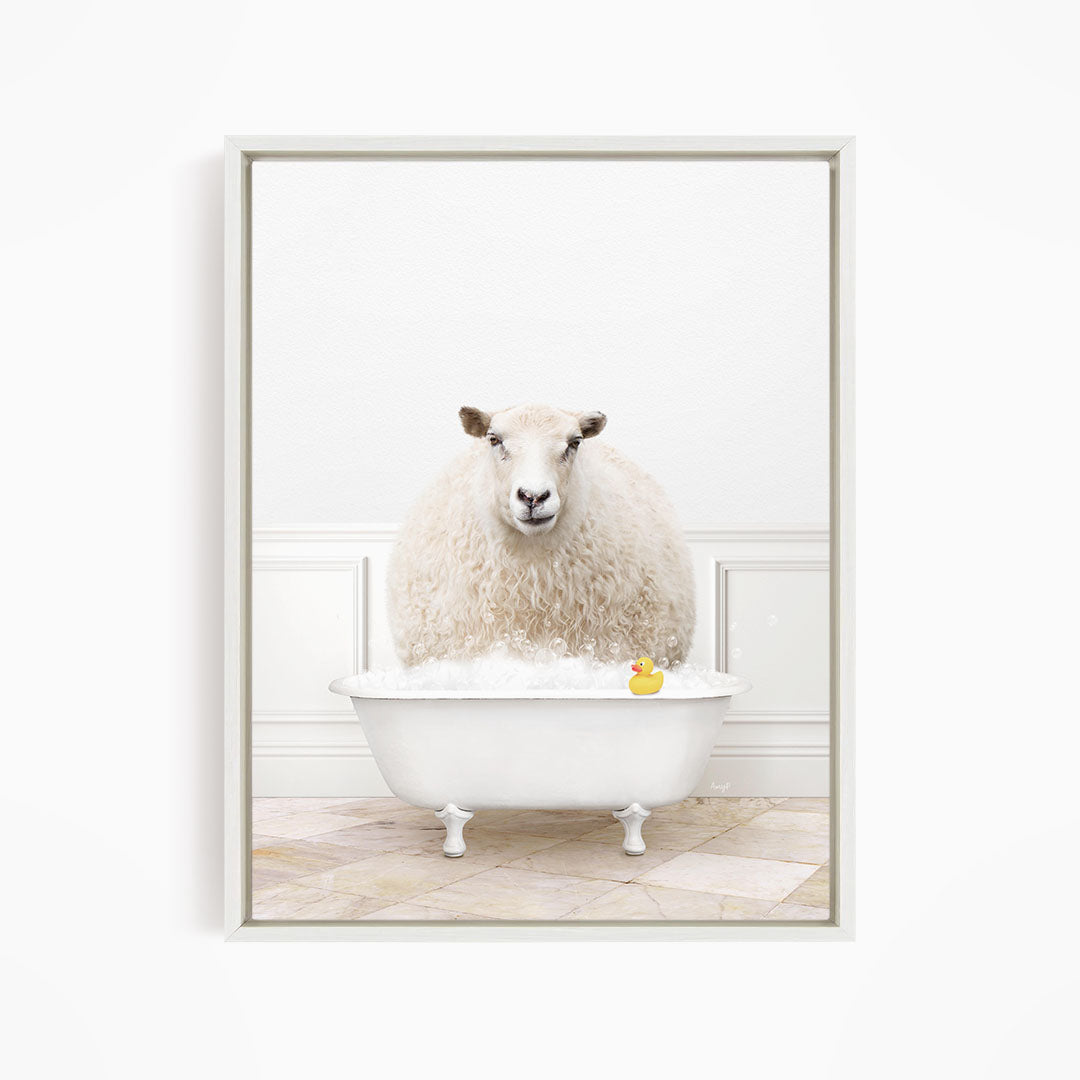 A fluffy white sheep sits in a white bathtub filled with bubbles, with a yellow rubber duck floating in the water.