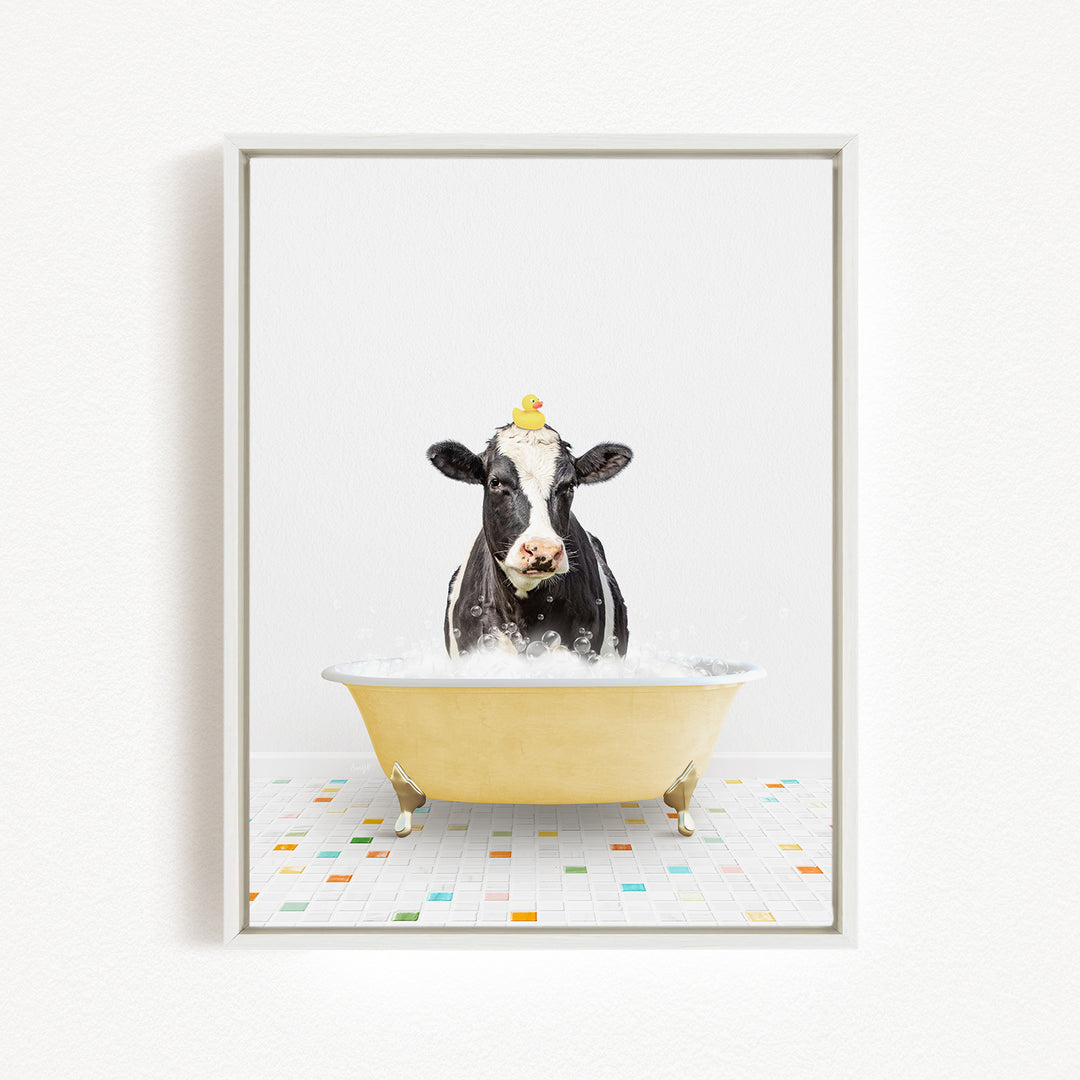 A black and white cow is sitting in a yellow bathtub filled with bubbles, with a yellow rubber duck perched on its head.