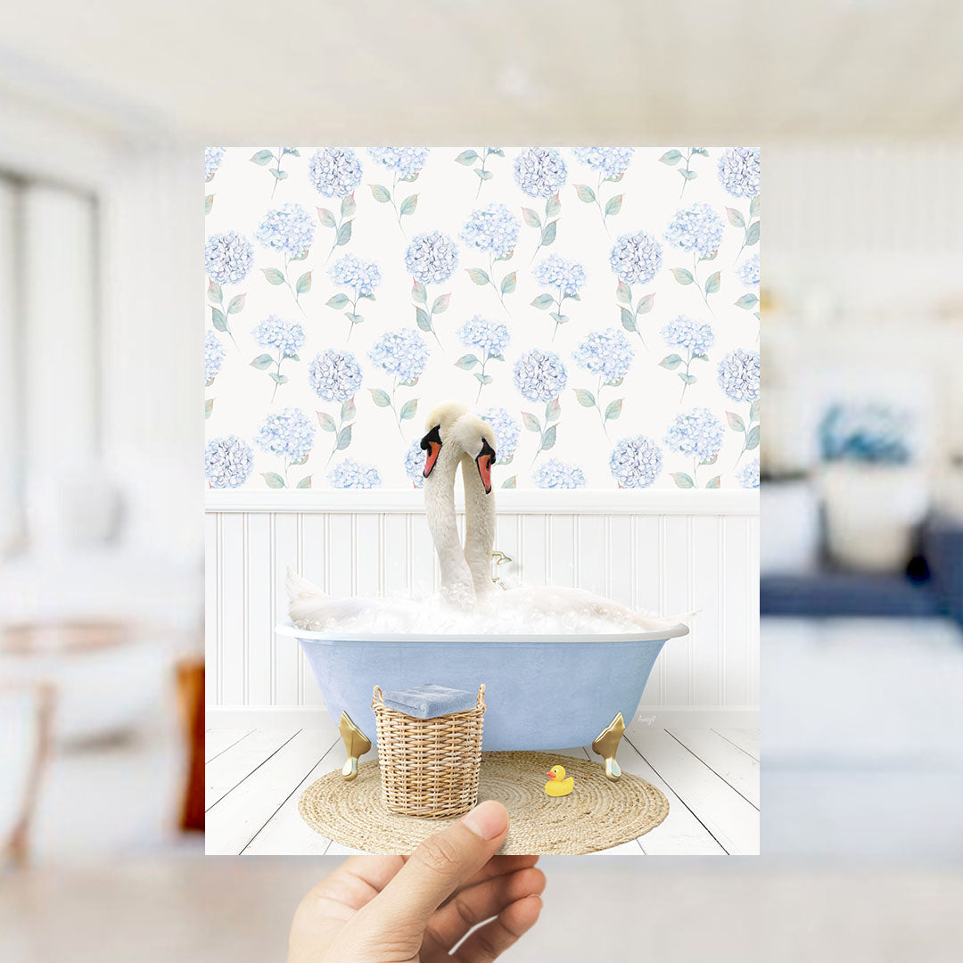 A hand holds up a photograph of a blue bathtub with two swans sitting in it, surrounded by a floral patterned wall.