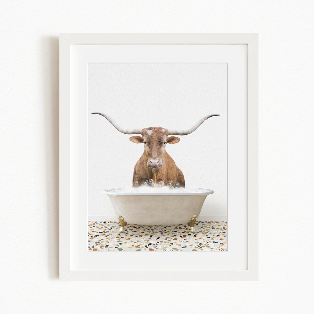 A brown cow with long horns is sitting in a white bathtub filled with water, appearing to be enjoying a bath.