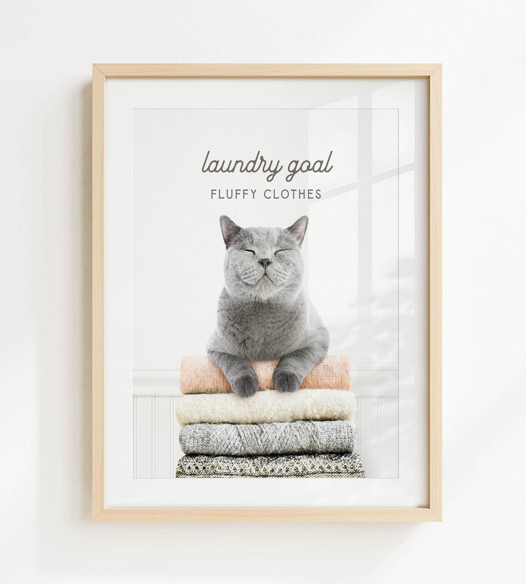 A gray cat sitting on a stack of clothes, with the text "laundry goal" and "fluffy clothes" written above it.