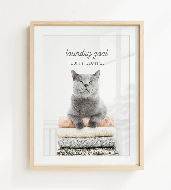 A gray cat sitting on a stack of clothes, with the text "laundry goal" and "fluffy clothes" written above it.