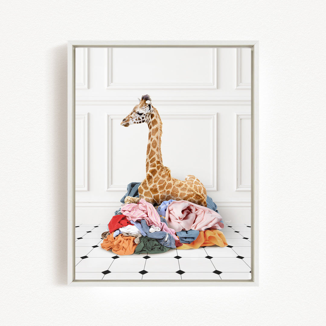 A giraffe is sitting on a pile of clothes on a tiled floor, with a white wall and paneled wall in the background.