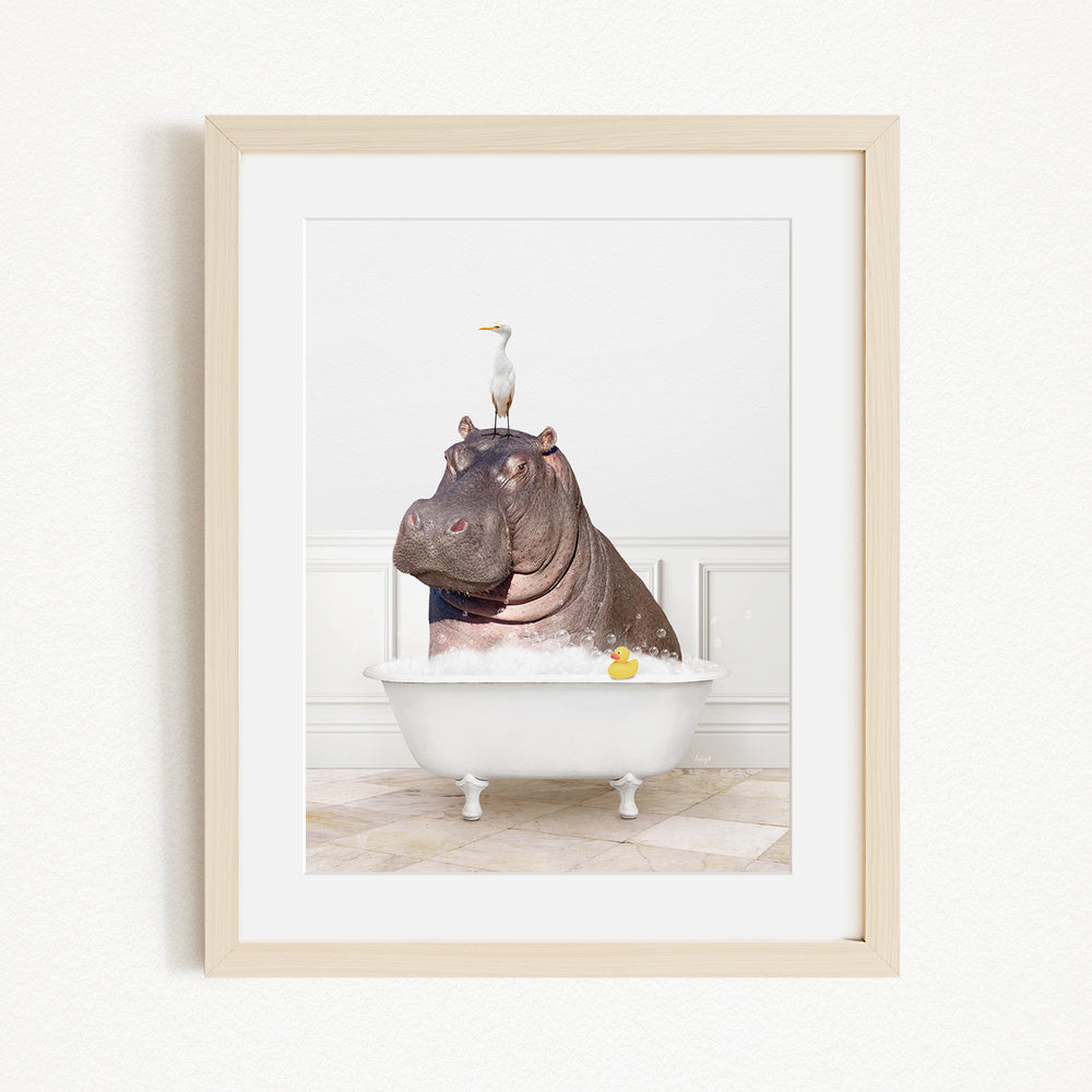 A framed image depicting a hippopotamus sitting in a bathtub, with a bird perched on its head.