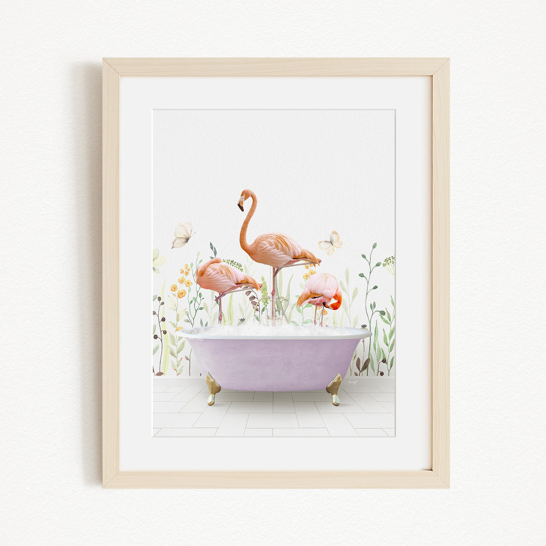 A framed illustration depicting three flamingos standing in a bathtub filled with bubbles, surrounded by a garden-like setting with flowers and butterflies.