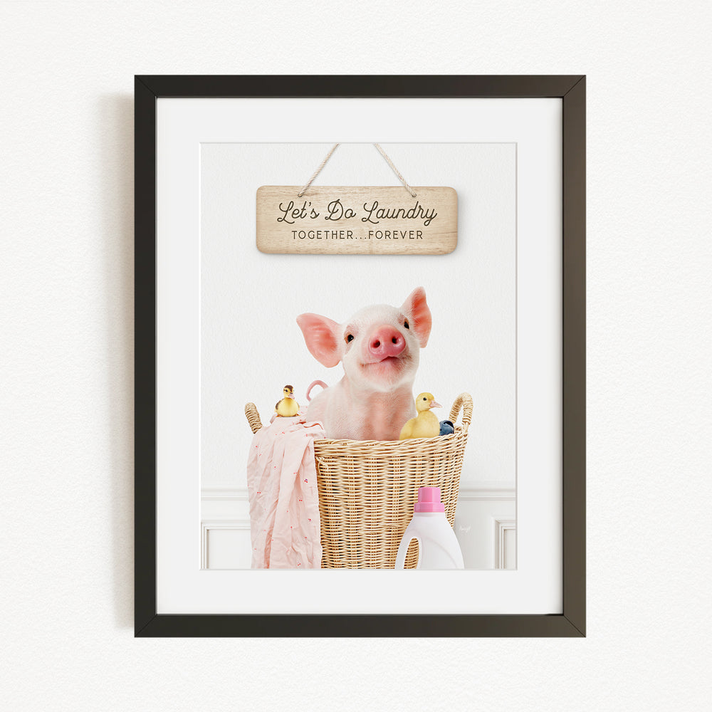 A framed image of a pig sitting in a wicker basket filled with rubber ducks, accompanied by a wooden sign that reads "Let's Do Laundry Together Forever".