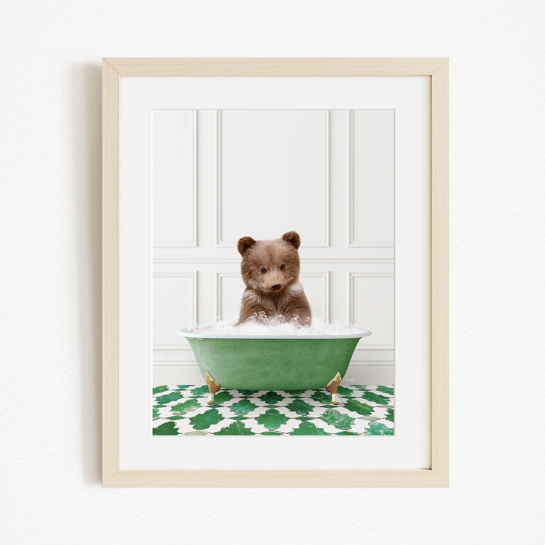 A small brown bear cub sitting in a green bathtub filled with water, surrounded by a green and white patterned rug.