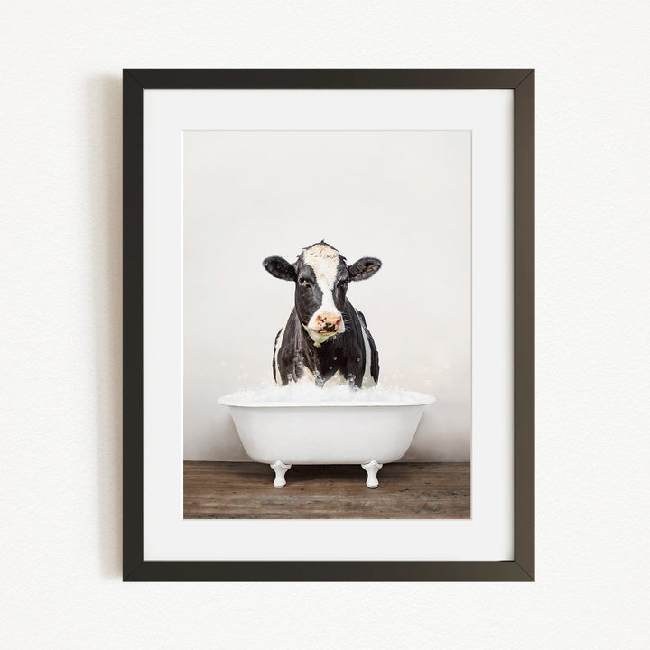 A black and white cow is standing in a white bathtub filled with water, creating a humorous and whimsical scene.