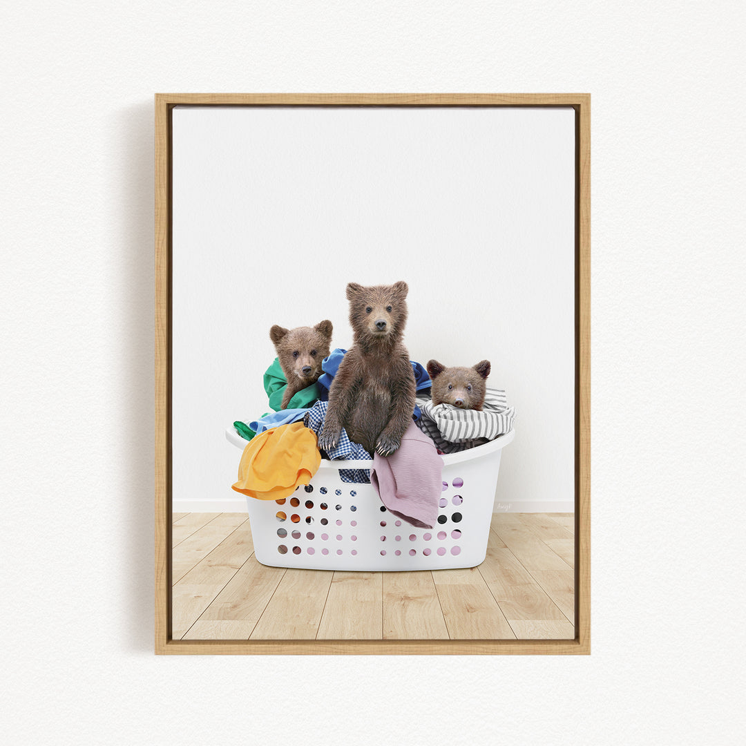 Three brown bears sitting in a white laundry basket filled with clothes.