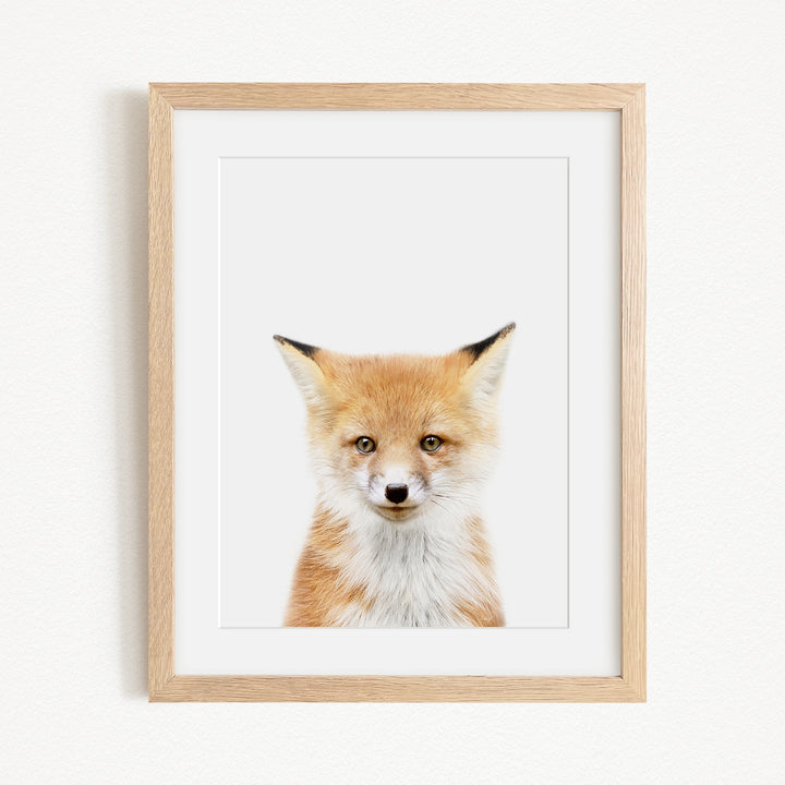 A framed print of a fox's face is displayed on a white wall.