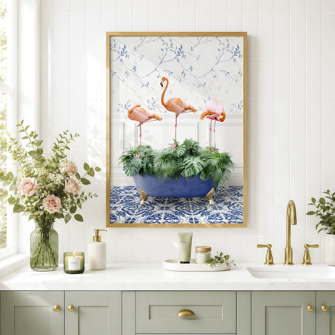 a bathroom with a framed picture of three flamingos standing in a bathtub filled with green plants. The bathroom has white tiles and a white countertop with various toiletries and decorative items.