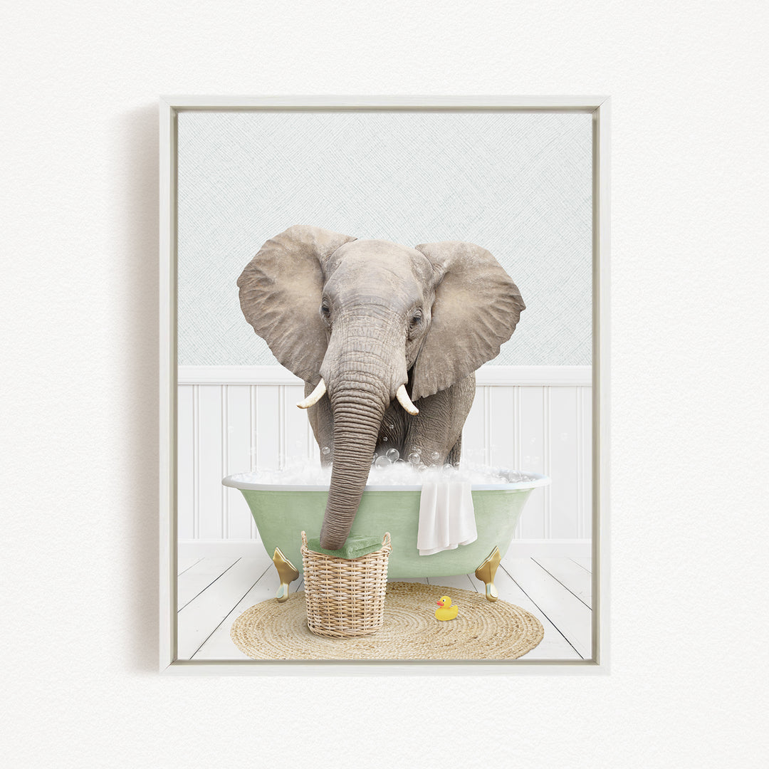 An elephant is sitting in a green bathtub filled with water, surrounded by a basket of toys and a yellow rubber duck.