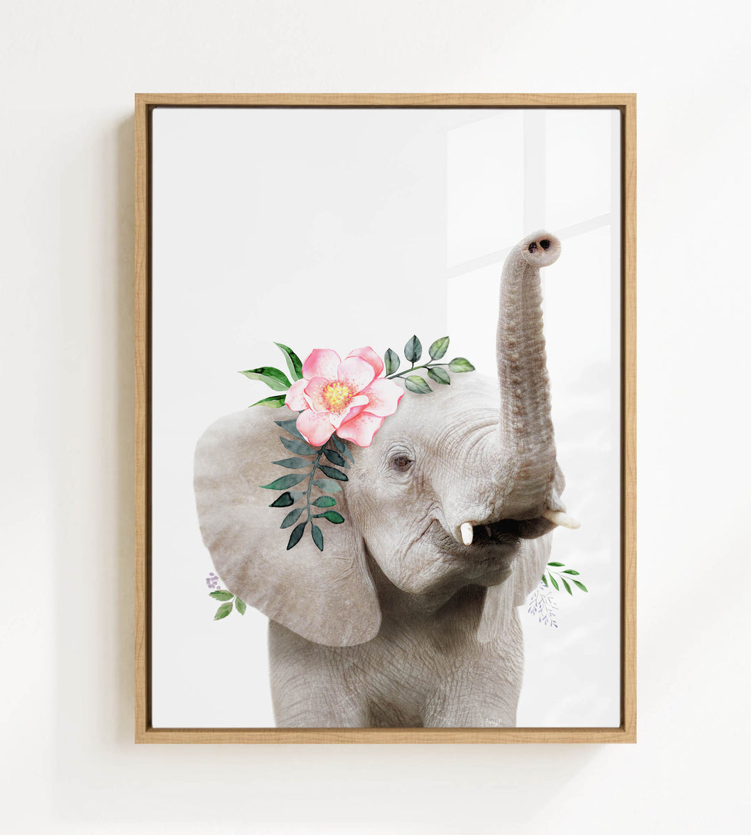A framed image of an elephant with a pink flower on its head and green leaves.