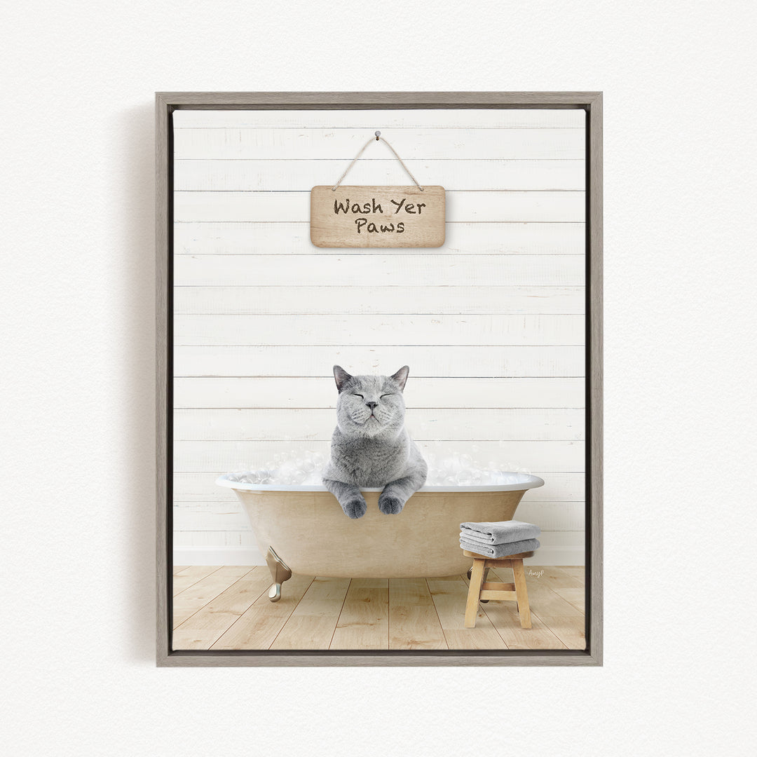 A gray cat sitting in a bathtub filled with bubbles, with a sign above that says "Wash Yer Paws".
