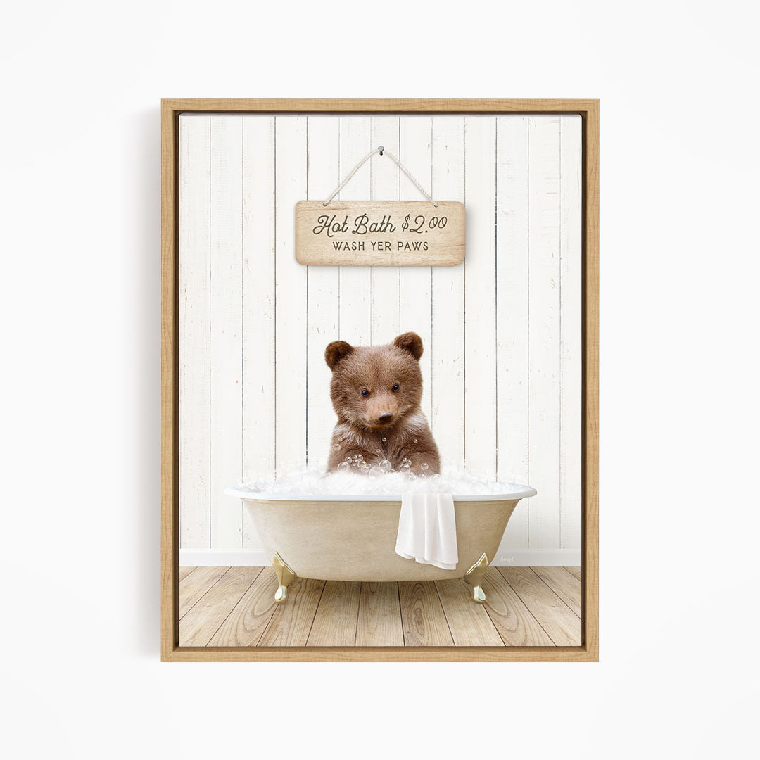 A brown bear sitting in a white bathtub, with a wooden sign above it that reads "Hot Bath $2.00 WASH YER Paws".