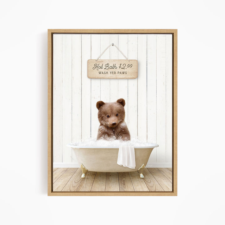 A brown bear sitting in a white bathtub, with a wooden sign above it that reads "Hot Bath $2.00 WASH YER Paws".