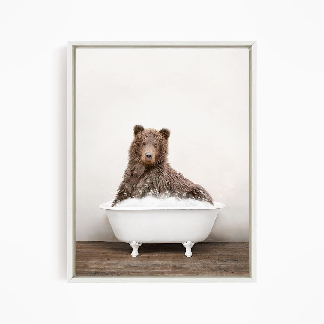 A brown bear sitting in a white bathtub filled with water, looking directly at the camera.
