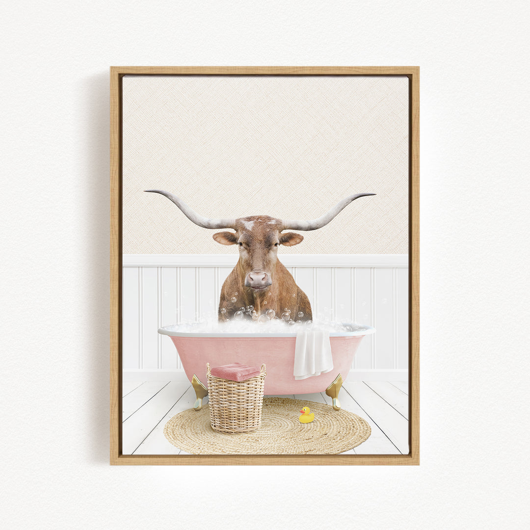 A brown bull with long horns is sitting in a pink bathtub filled with bubbles, surrounded by a basket of toys and a yellow rubber duck.