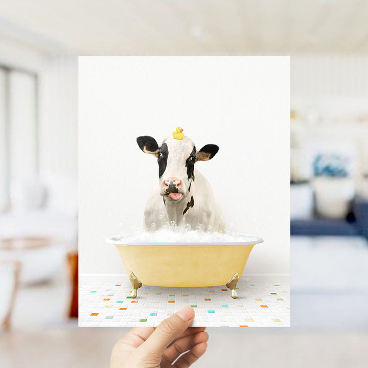 A cow is sitting in a yellow bathtub filled with bubbles, with a rubber duck perched on its head.