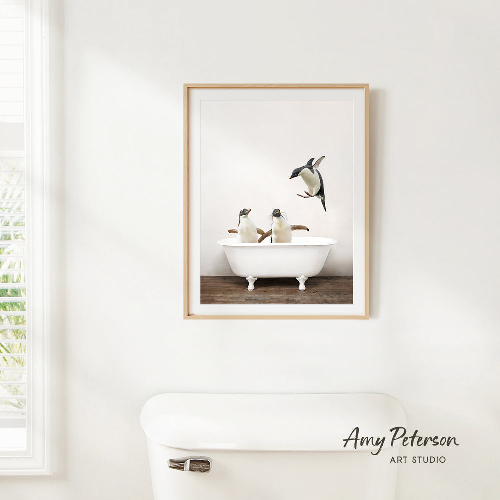 A framed image of three penguins sitting in a white bathtub, with one penguin standing on the edge of the tub.